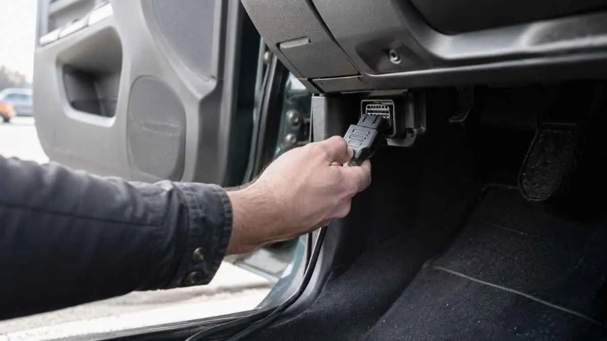 Person plugging an OBD2 scanner into a used car's diagnostic port before purchase